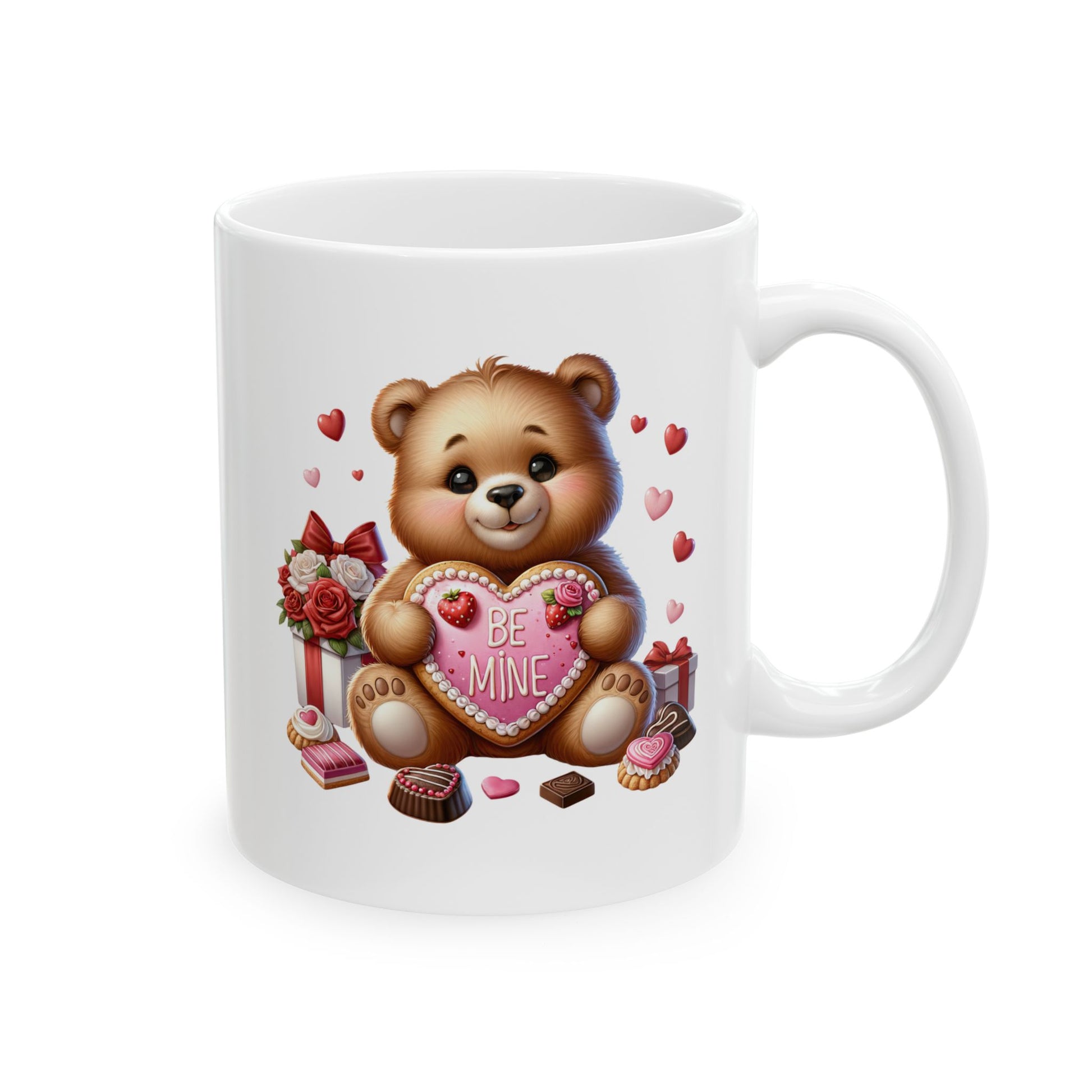 White ceramic coffee mug with a cute cartoon teddy bear holding a pink heart-shaped cookie that says 'BE MINE', surrounded by red hearts, chocolate candies, and wrapped gifts