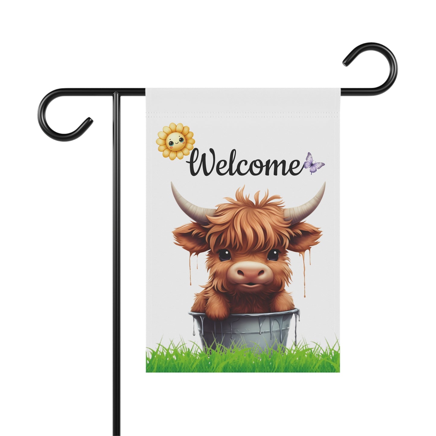 Fluffy baby Highland cow sitting inside a bucket on green grass under Welcome text with a sunflower and purple butterfly garden flag