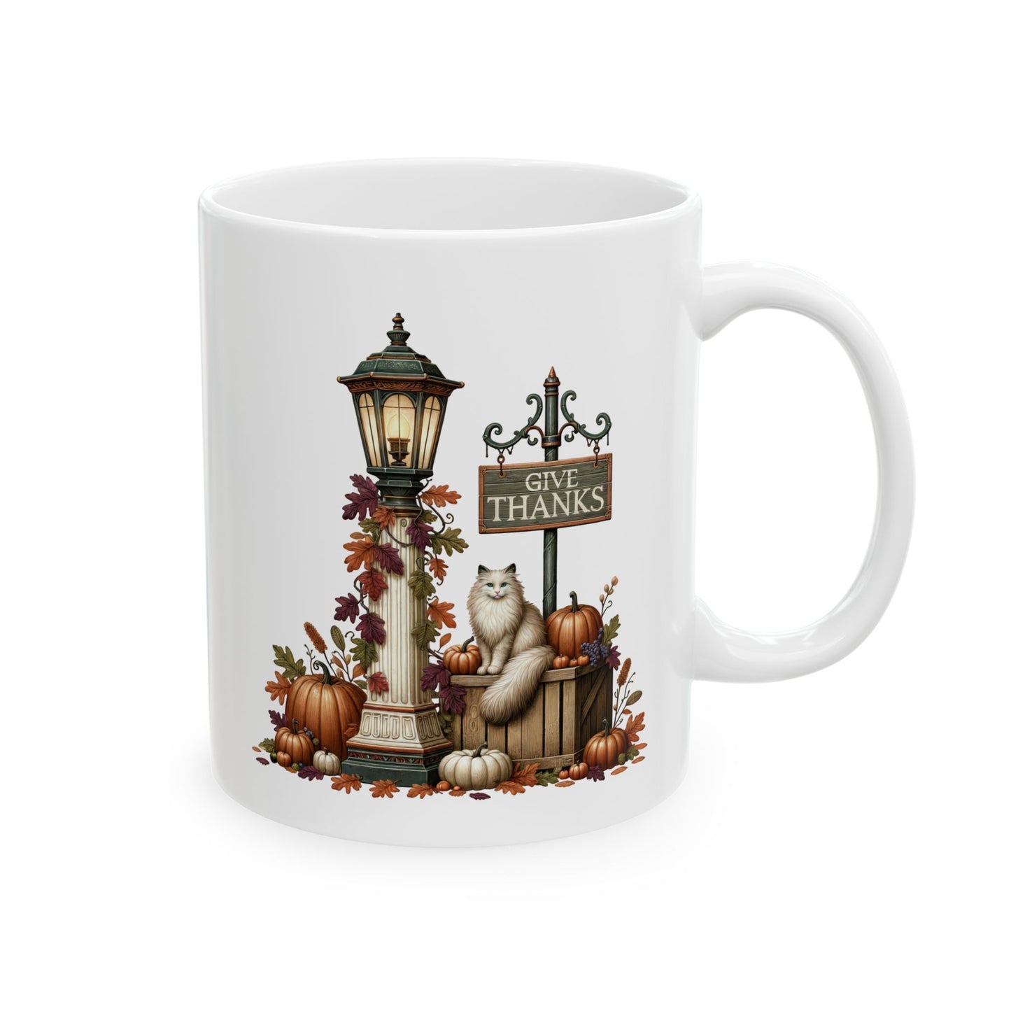 White ceramic coffee mug featuring an illustration of a fluffy long-haired cat sitting on a wooden crate next to a glowing lamppost, pumpkins, and a sign that reads Give Thanks.