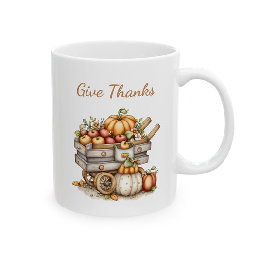 Give Thanks ceramic coffee mug featuring a cute illustration of a rustic wooden wagon filled with apples and a large pumpkin, with additional pumpkins underneath on the ground, under warm brown text.
