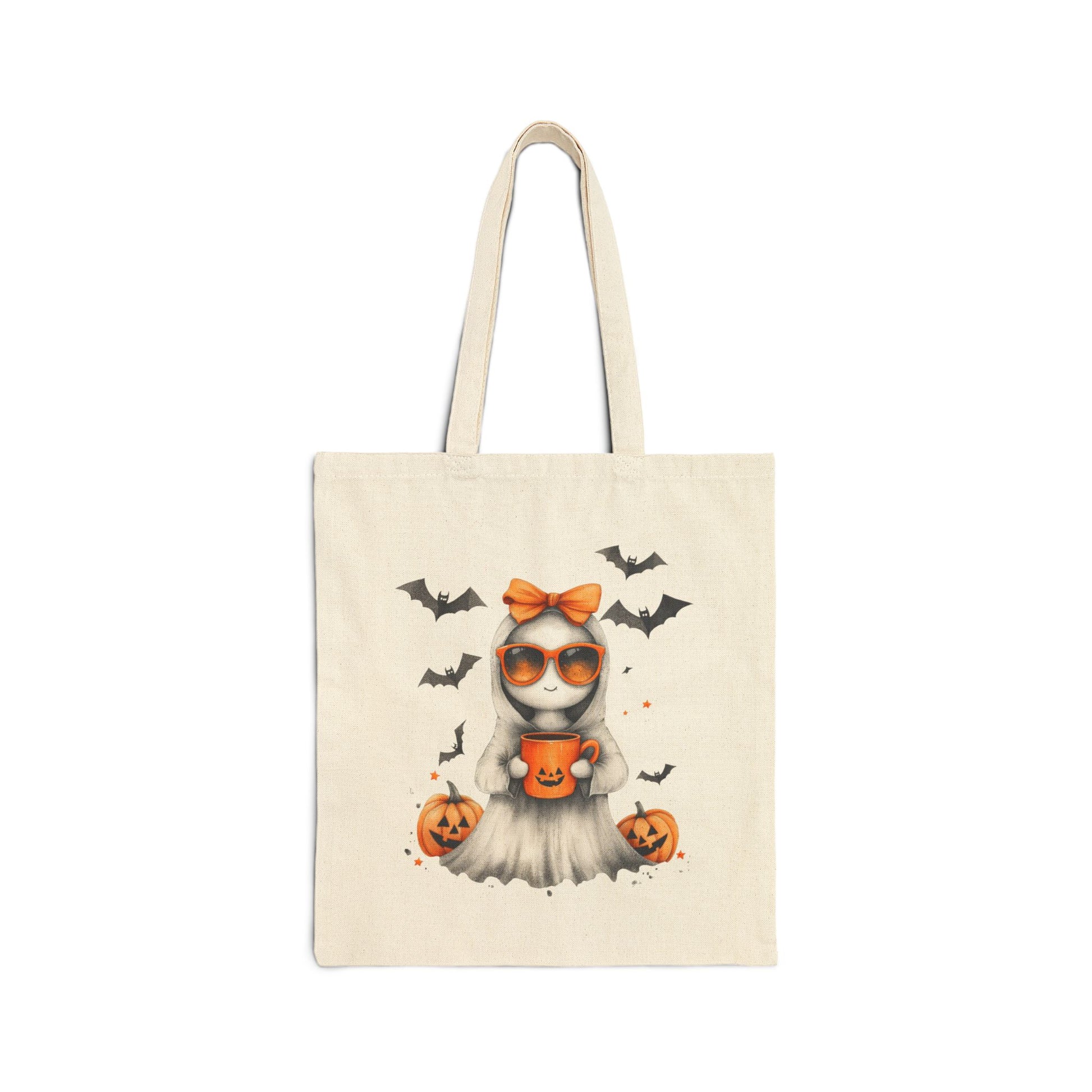 A cream-colored canvas tote bag featuring a cute ghost illustration wearing orange sunglasses and an orange bow, holding a pumpkin mug. Bats are flying in the background, and pumpkins are on the ground.