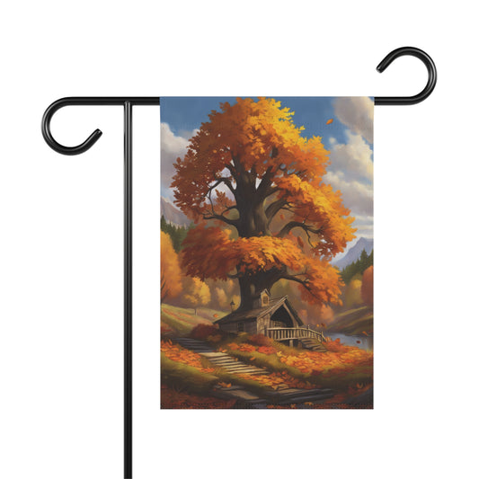 Garden flag depicting a scenic autumn landscape with a large, vibrant orange-leafed tree towering over a small rustic cabin next to water, with distant mountains and fallen leaves on the ground.
