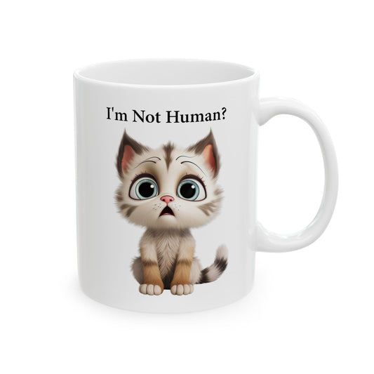 White ceramic coffee mug with a cartoon illustration of a cute, slightly sad or bewildered brown and white tabby kitten with large blue-green eyes, and black text above reads "I'm Not Human?".