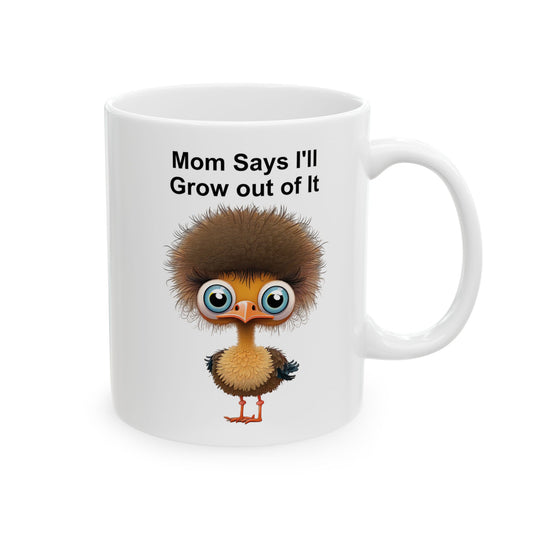 White ceramic coffee mug with a cartoon ostrich illustration with fluffy brown hair and big blue eyes, and the text "Mom Says I'll Grow Out of It" above it