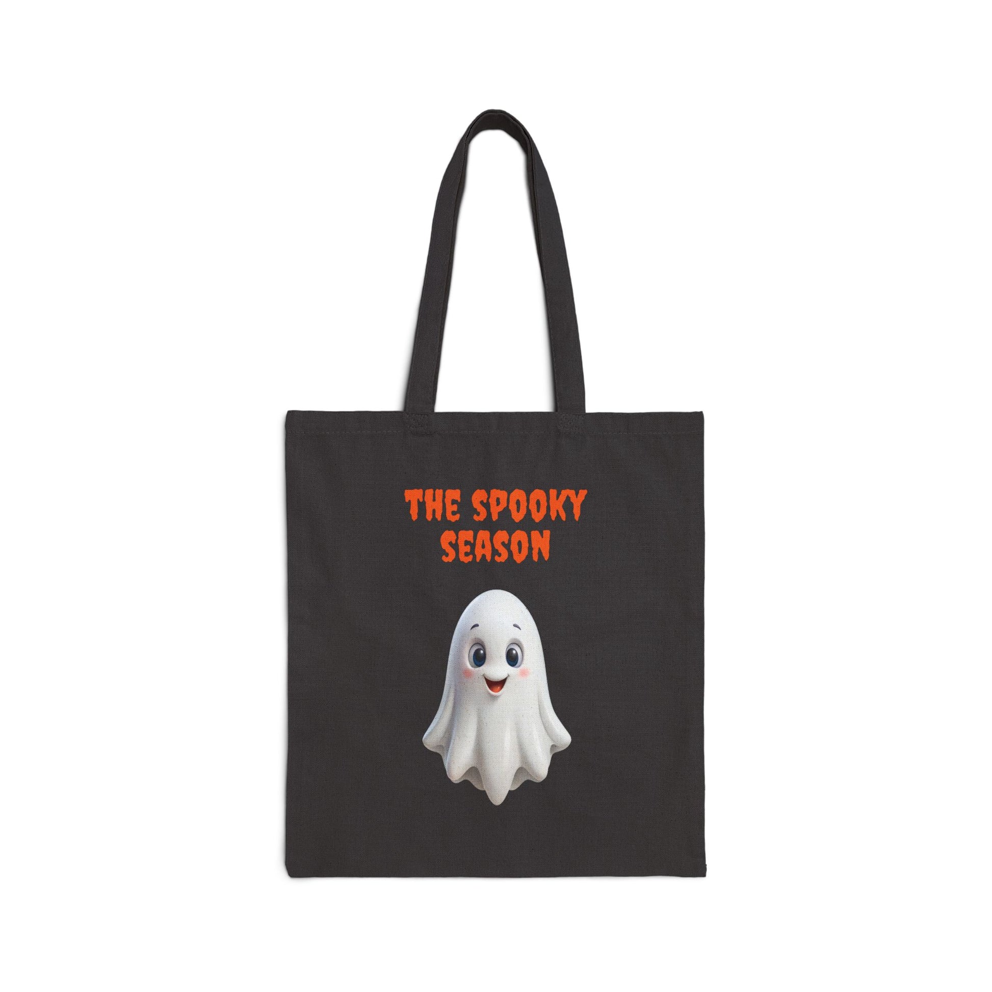 A black 100% cotton canvas tote bag featuring an illustration of a cute white ghost with large, round eyes. The text "THE SPOOKY SEASON" is printed in orange above the ghost.
