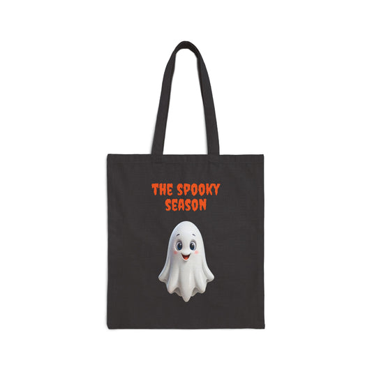A black 100% cotton canvas tote bag featuring an illustration of a cute white ghost with large, round eyes. The text "THE SPOOKY SEASON" is printed in orange above the ghost.