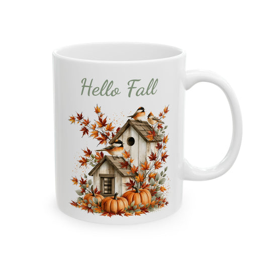 White ceramic mug featuring fall songbird and birdhouse artwork beneath green script text reading Hello Fall.
