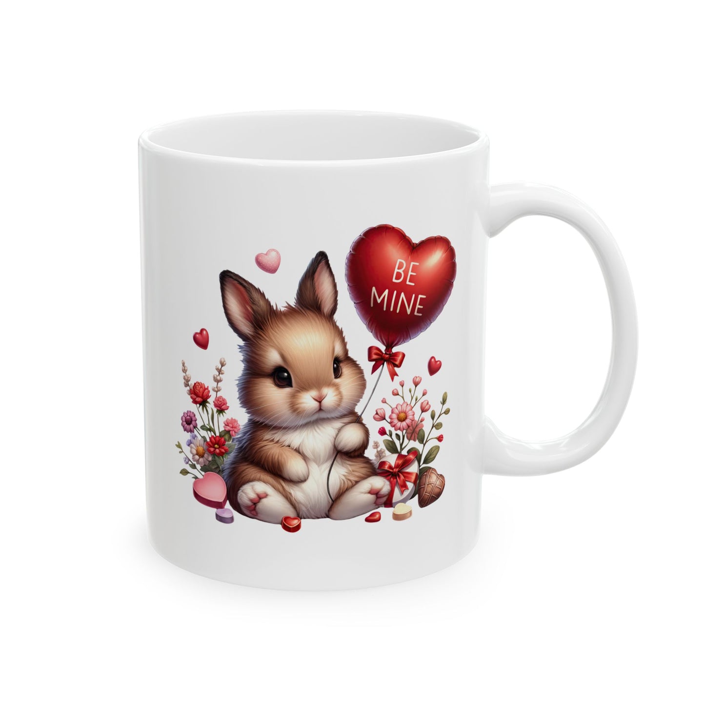 White ceramic coffee mug with a cute cartoon baby bunny holding a red heart-shaped balloon that says 'BE MINE', surrounded by pink and red flowers, small hearts, and chocolates.
