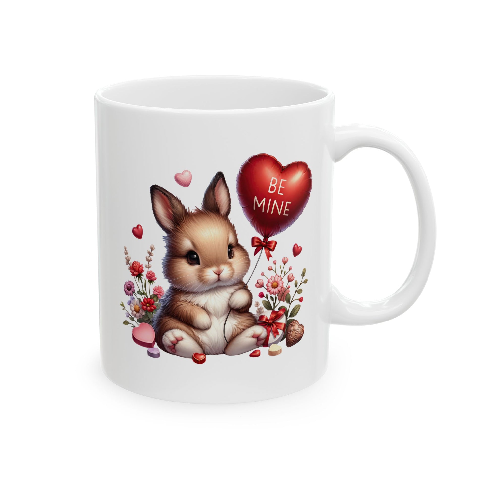White ceramic coffee mug with a cute cartoon baby bunny holding a red heart-shaped balloon that says 'BE MINE', surrounded by pink and red flowers, small hearts, and chocolates.
