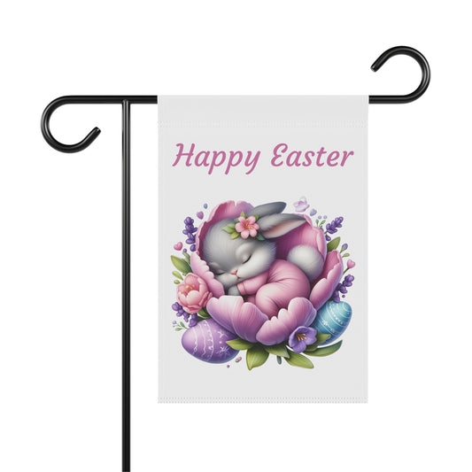 White garden flag with the text "Happy Easter" in pink, featuring a cute gray cartoon bunny sleeping peacefully curled up inside a large purple and pink flower, surrounded by lavender sprigs and colorful patterned Easter eggs. The flag is displayed on a black metal garden flag stand.

