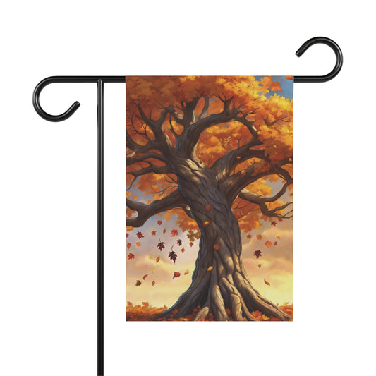 Garden flag depicting a large, old tree with vibrant orange and yellow autumn leaves, with many leaves falling around its trunk. The ground below is covered in fallen leaves. 