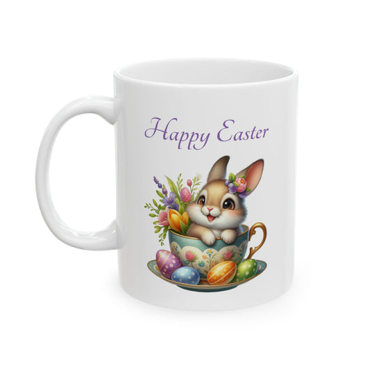 White ceramic mug with "Happy Easter" text, featuring a cute brown cartoon bunny sitting in a light blue teacup with a floral design, surrounded by colorful flowers and painted Easter eggs.

