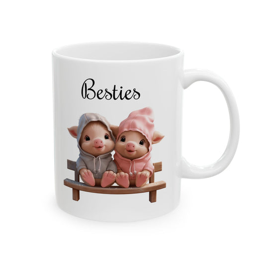 White ceramic coffee mug with two cute cartoon piglets in hoodies sitting on a bench, with the word "Besties" written above them.