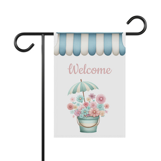 Spring garden flag featuring a pastel flower bucket topped with a striped miniature umbrella set beneath a blue and white striped awning border with pink script text reading Welcome.