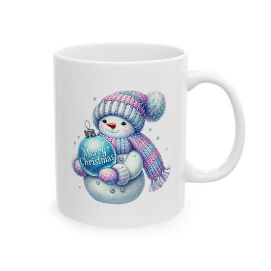 White ceramic coffee mug printed with an illustration of a cute snowman in a pink and blue knitted scarf and hat holding a blue Merry Christmas ornament
