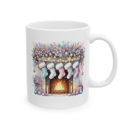 White ceramic coffee mug printed with an illustration of a cozy brick fireplace with glowing fire, hung pastel pink and blue stockings, and floral garland decor