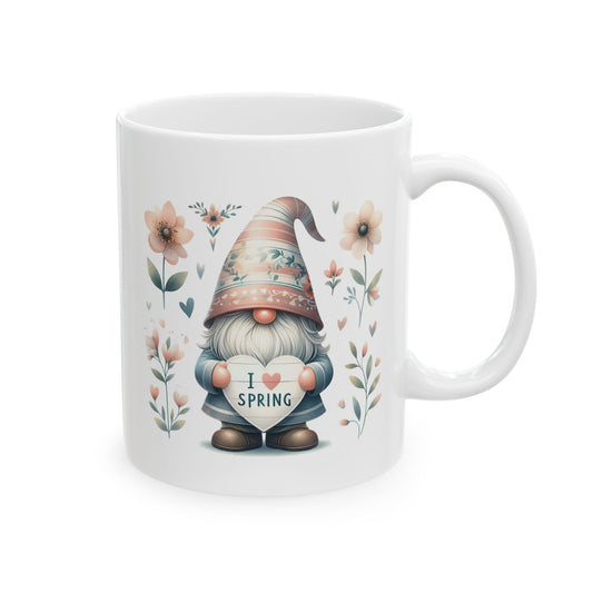 A white ceramic coffee mug with a watercolor illustration of a gnome holding a heart that says "I Love Spring," surrounded by flowers.

