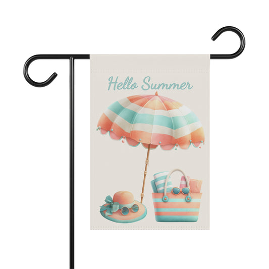 Summer garden flag featuring a pastel striped beach umbrella set above a sun hat and a tote bag packed with rolled towels and sunglasses under teal script text reading Hello Summer.