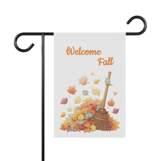 White vertical garden flag on a black metal hanger featuring a soft illustration of a wooden rake leaning against a pile of colorful autumn leaves under the words Welcome Fall in orange script.