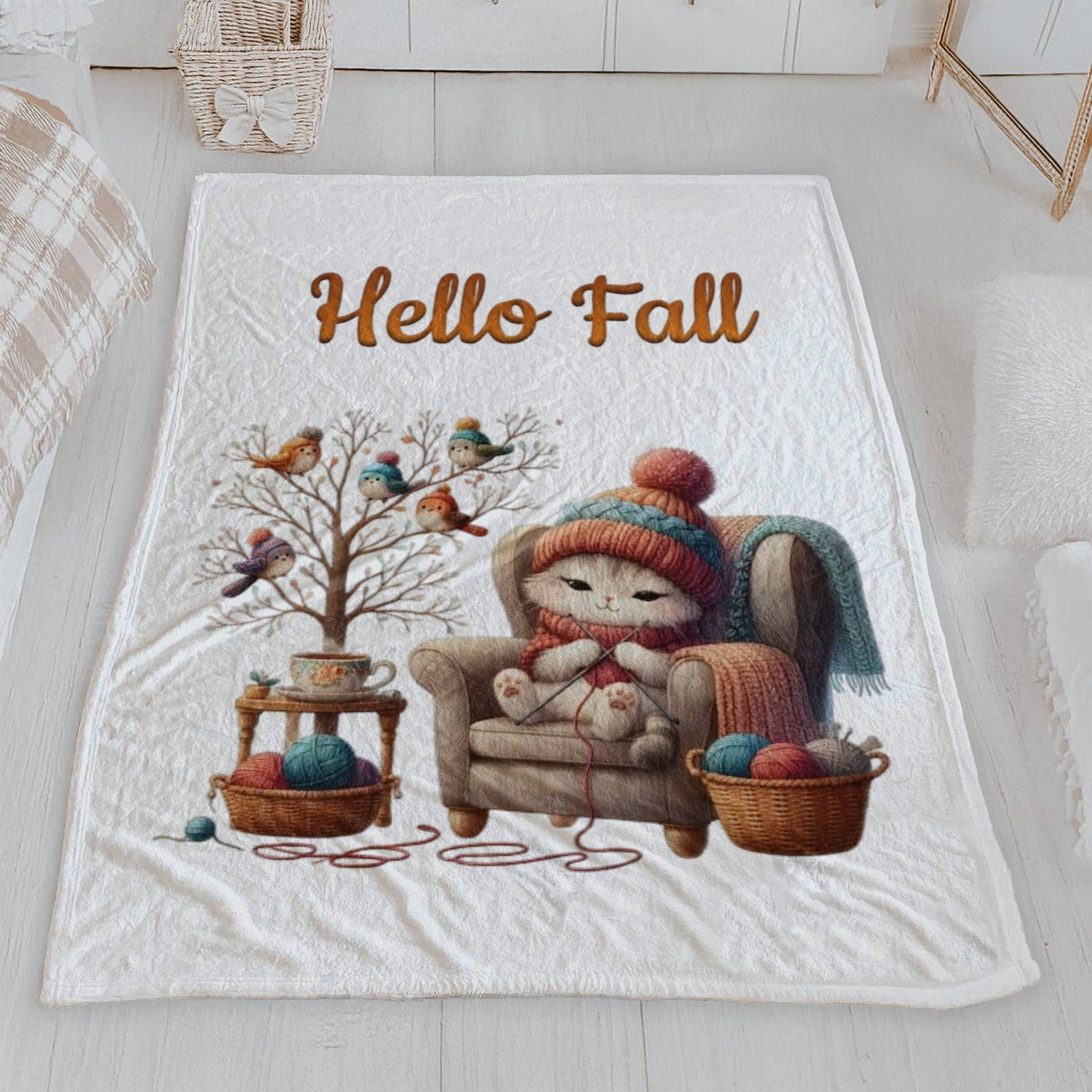 White velveteen blanket with a cozy autumn illustration of a cute cat knitting in an armchair, with birds in hats on a bare tree, and the words "Hello Fall" in orange script text above the scene.

